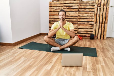 Photo for Handsome hispanic man meditating with video tutorial on laptop at the gym - Royalty Free Image