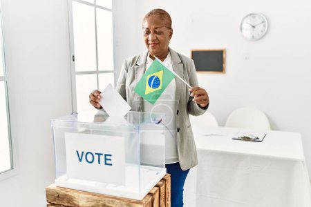 Foto de Mujer afroamericana mayor con bandera brasileña votando en colegio electoral - Imagen libre de derechos