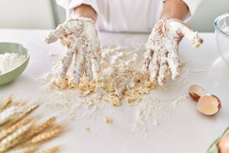 Foto de Young woman wearing cook uniform kneading flour at kitchen - Imagen libre de derechos
