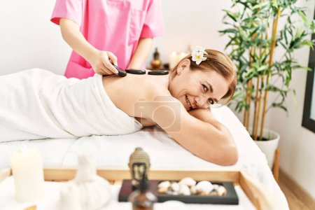 Photo for Middle age caucasian woman having back massage using hot stones at beauty center - Royalty Free Image