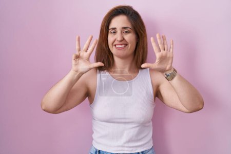 Foto de Mujer morena de pie sobre fondo rosa mostrando y señalando hacia arriba con los dedos número nueve mientras sonríe confiado y feliz. - Imagen libre de derechos