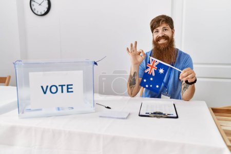 Foto de Hombre caucásico con barba larga en las elecciones de campaña política sosteniendo la bandera de Australia haciendo buen signo con los dedos, sonriendo gesto amistoso excelente símbolo - Imagen libre de derechos