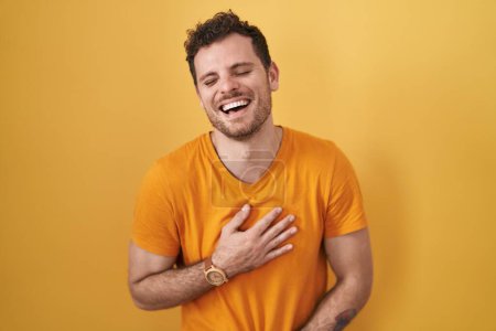 Photo for Young hispanic man standing over yellow background smiling and laughing hard out loud because funny crazy joke with hands on body. - Royalty Free Image