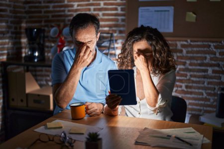 Photo for Middle age hispanic couple using touchpad sitting on the table at night tired rubbing nose and eyes feeling fatigue and headache. stress and frustration concept. - Royalty Free Image