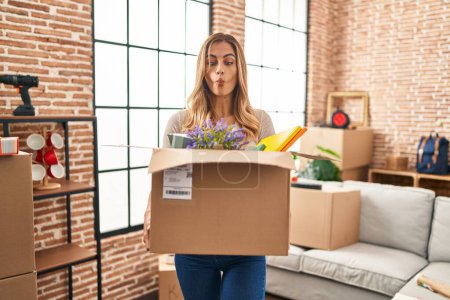 Photo for Young blonde woman moving to a new home holding cardboard box making fish face with mouth and squinting eyes, crazy and comical. - Royalty Free Image
