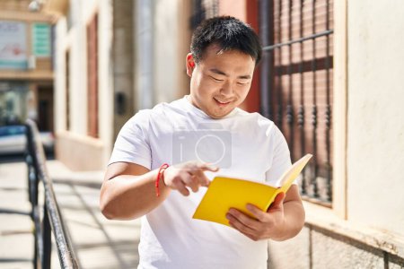 Téléchargez les photos : Jeune Chinois souriant livre de lecture confiant à la rue - en image libre de droit
