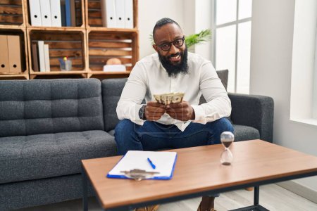 Photo for Young african american man psychologist counting dollars at psychology center - Royalty Free Image