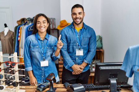 Photo for Young interracial people working at retail boutique showing and pointing up with finger number one while smiling confident and happy. - Royalty Free Image