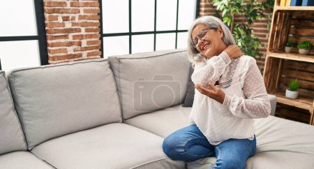 Foto de Mujer de mediana edad sentada en el sofá sufriendo de dolor de cuello en casa - Imagen libre de derechos