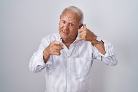 Photo for Senior man with grey hair standing over isolated background smiling doing talking on the telephone gesture and pointing to you. call me. - Royalty Free Image