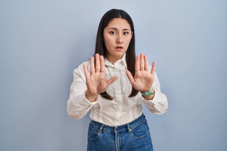 Photo for Young latin woman standing over blue background moving away hands palms showing refusal and denial with afraid and disgusting expression. stop and forbidden. - Royalty Free Image