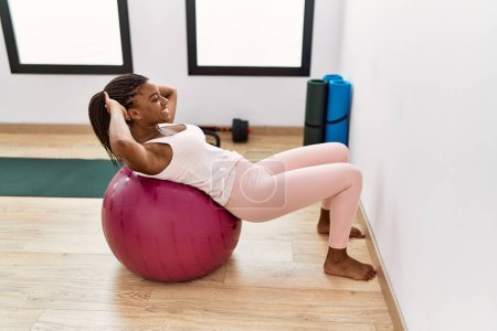 Photo for Young african american woman smiling confident training abs exersice with fit ball at sport center - Royalty Free Image