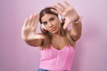 Foto de Young blonde woman listening to music using headphones doing frame using hands palms and fingers, camera perspective - Imagen libre de derechos