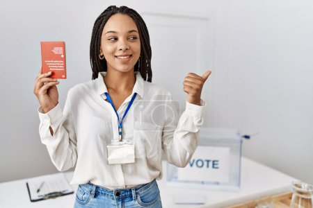 Photo for Young african american woman at political campaign election holding swiss passport pointing thumb up to the side smiling happy with open mouth - Royalty Free Image