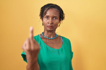 Foto de African woman with dreadlocks standing over yellow background showing middle finger, impolite and rude fuck off expression - Imagen libre de derechos