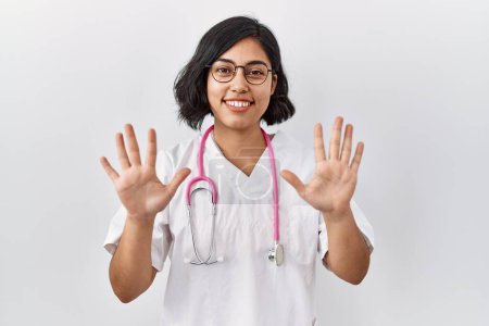 Foto de Joven doctora hispana usando estetoscopio sobre fondo aislado mostrando y señalando con los dedos el número diez mientras sonríe confiada y feliz. - Imagen libre de derechos