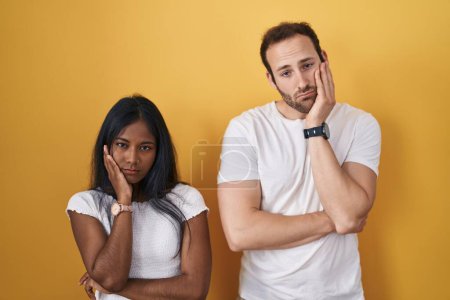 Téléchargez les photos : Couple Interracial debout sur fond jaune pensant fatigué et ennuyé avec des problèmes de dépression avec les bras croisés. - en image libre de droit