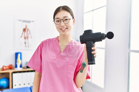 Foto de Joven mujer asiática sosteniendo arma muscular en fisioterapia clínica - Imagen libre de derechos