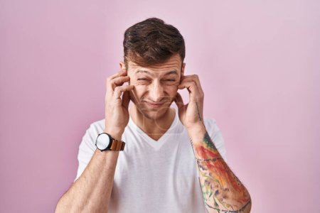 Téléchargez les photos : Caucasian man standing over pink background covering ears with fingers with annoyed expression for the noise of loud music. deaf concept. - en image libre de droit