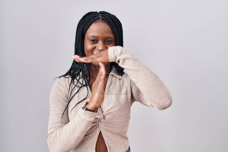 Téléchargez les photos : Femme africaine avec des tresses debout sur fond blanc faire le temps geste avec les mains, visage frustré et sérieux - en image libre de droit