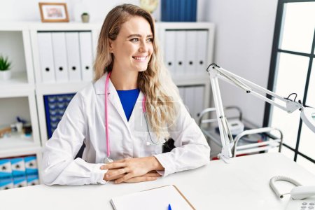 Foto de Young woman wearing doctor uniform smiling confident at clinic - Imagen libre de derechos
