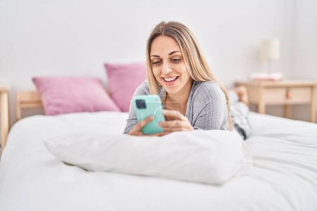 Photo for Young woman using smartphone lying on bed at bedroom - Royalty Free Image
