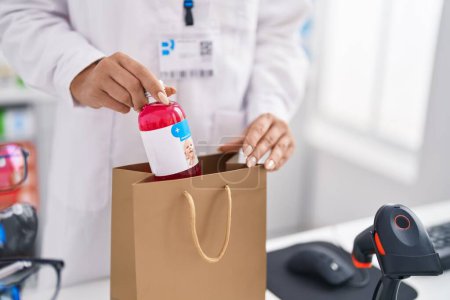 Photo for Young blonde woman pharmacist putting medication bottle on shopping bag at pharmacy - Royalty Free Image