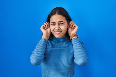 Photo for Young brazilian woman standing over blue isolated background covering ears with fingers with annoyed expression for the noise of loud music. deaf concept. - Royalty Free Image