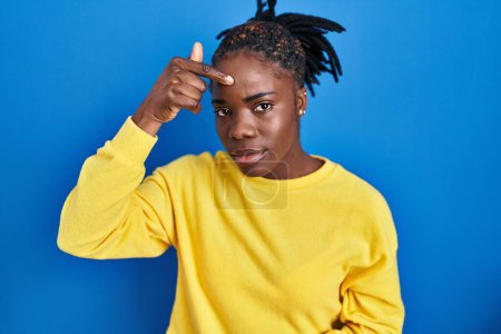 Photo for Beautiful black woman standing over blue background pointing unhappy to pimple on forehead, ugly infection of blackhead. acne and skin problem - Royalty Free Image