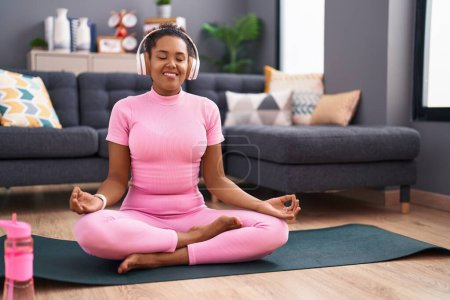 Foto de African american woman listening to music doing yoga exercise at home - Imagen libre de derechos