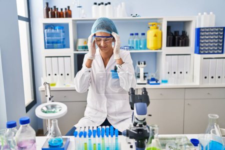 Téléchargez les photos : Brunette woman working at scientist laboratory with hand on head, headache because stress. suffering migraine. - en image libre de droit