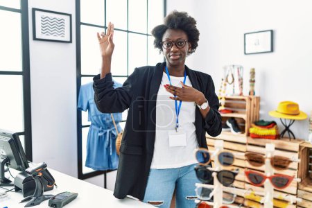 Photo for African young woman working as manager at retail boutique smiling swearing with hand on chest and fingers up, making a loyalty promise oath - Royalty Free Image