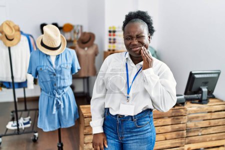 Foto de Mujer africana joven que trabaja como gerente en boutique minorista tocando la boca con la mano con expresión dolorosa debido a dolor de muelas o enfermedades dentales en los dientes. dentista - Imagen libre de derechos
