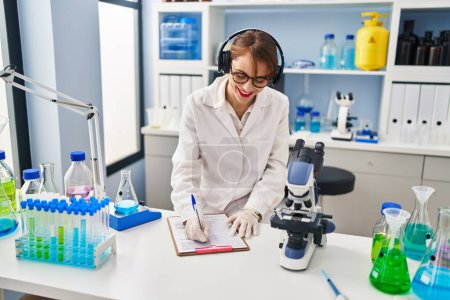 Photo for Young caucasian woman wearing scientist uniform listening to music working at laboratory - Royalty Free Image