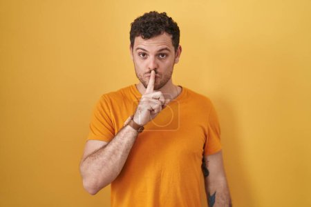 Photo for Young hispanic man standing over yellow background asking to be quiet with finger on lips. silence and secret concept. - Royalty Free Image
