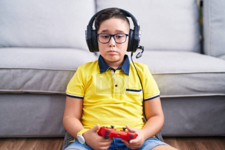 Photo for Young hispanic kid playing video game holding controller wearing headphones depressed and worry for distress, crying angry and afraid. sad expression. - Royalty Free Image