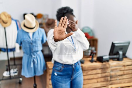 Téléchargez les photos : Jeune femme africaine travaillant comme directrice à la boutique de détail couvrant les yeux avec les mains et faisant un geste d'arrêt avec expression triste et peur. concept embarrassé et négatif. - en image libre de droit