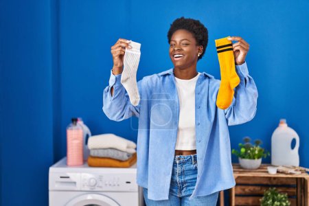 Foto de Afro americana mujer sosteniendo limpio andy sucio calcetines sonriendo y riendo duro en voz alta porque divertido loco broma. - Imagen libre de derechos