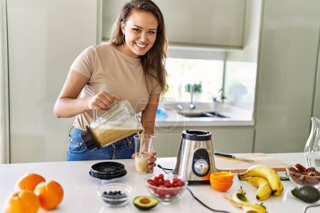 Téléchargez les photos : Young beautiful hispanic woman smiling confident pouring vegetable smoothie on glass at the kitchen - en image libre de droit