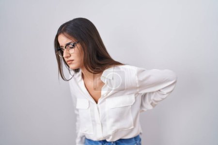 Téléchargez les photos : Jeune femme brune portant des lunettes souffrant de maux de dos, toucher le dos avec la main, douleur musculaire - en image libre de droit