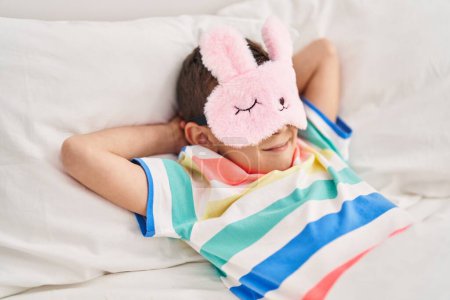 Téléchargez les photos : Enfant blond portant un masque de sommeil couché sur le lit dans la chambre - en image libre de droit