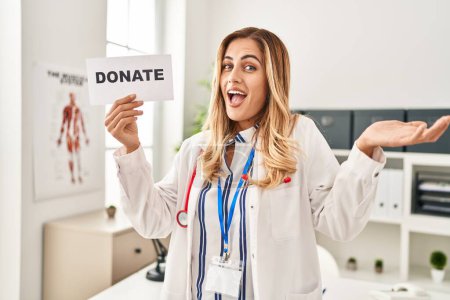 Téléchargez les photos : Jeune femme blonde médecin soutenant les dons d'organes célébrant la réalisation avec un sourire heureux et l'expression gagnante avec la main levée - en image libre de droit