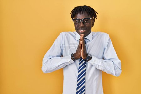 Téléchargez les photos : Homme africain avec dreadlocks debout sur fond jaune mendier et prier avec les mains ainsi que l'expression de l'espoir sur le visage très émotionnel et inquiet. mendier. - en image libre de droit