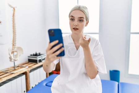 Photo for Young caucasian woman wearing physio therapist uniform having video call at clinic - Royalty Free Image