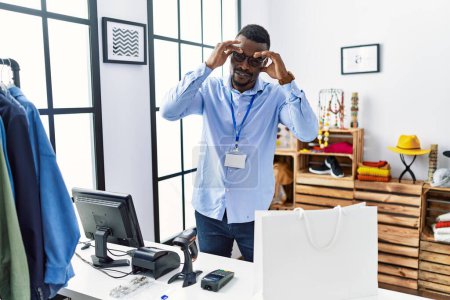 Foto de Joven hombre africano que trabaja como gerente en la boutique al por menor tratando de abrir los ojos con los dedos, soñoliento y cansado para la fatiga de la mañana - Imagen libre de derechos