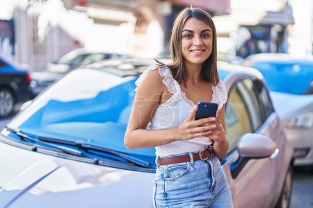 Téléchargez les photos : Jeune belle femme hispanique à l'aide d'un smartphone appuyé sur la voiture à la rue - en image libre de droit