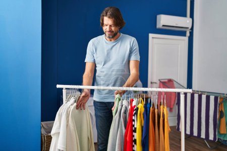 Photo for Middle age man smiling confident holding clothes on rack at laundry room - Royalty Free Image