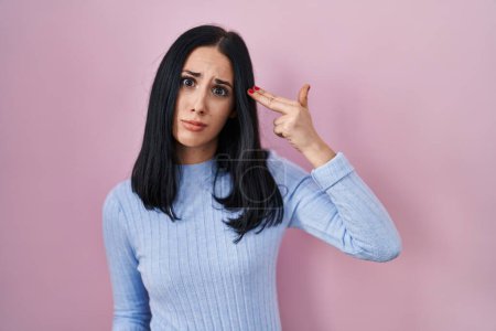 Photo for Hispanic woman standing over pink background shooting and killing oneself pointing hand and fingers to head like gun, suicide gesture. - Royalty Free Image