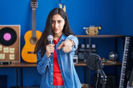 Foto de Young teenager girl singing song using microphone pointing with finger to the camera and to you, confident gesture looking serious - Imagen libre de derechos