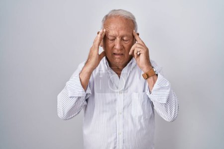Foto de Hombre mayor con el pelo gris de pie sobre el fondo aislado con la mano en la cabeza, dolor de cabeza porque el estrés. padecer migraña. - Imagen libre de derechos